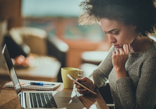 A young woman reads about safety and security measures online on her cellphone. A young woman reads tips to help spot scams and frauds on her mobile phone.